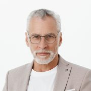 Portrait of smart and handsome intelligent senior male professor in stylish suit and glasses holding hands together against chest and gazing with self-assured wise expression at camera giving speech. Copy space